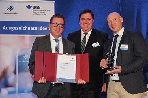 Dirk Dewald (li.) und Marcel Schlegel (re.) von der Nestlé Wagner GmbH freuen sich über die Auszeichnung. Hier bei der Preisübergabe mit dem Vorsitzenden des BGN-Präventionsausschusses Armin Juncker (Mitte).