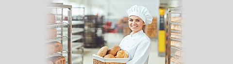 Lächelnde Bäckerin steht zwischen Regalen mit Backwaren in der Backstube